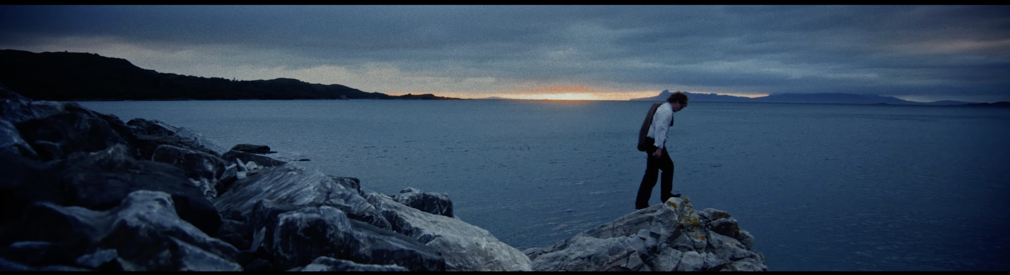 Film still — figure on rocks at sunset over the sea